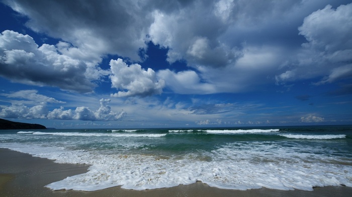 Waves crashing on a sandy beach under a cloudy sky