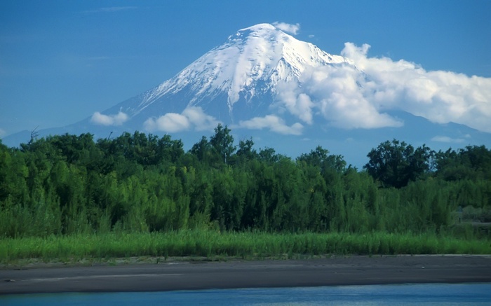 Snow-capped volcano over green forest and river