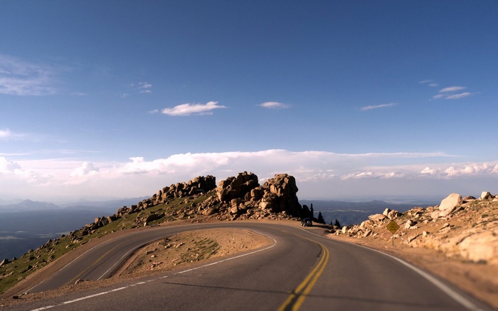 Winding mountain road with rocky peaks and blue sky