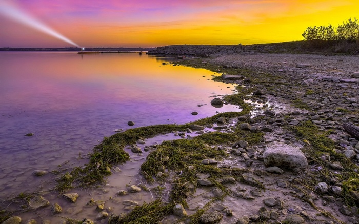 Sunset over a rocky shore with a lighthouse beam