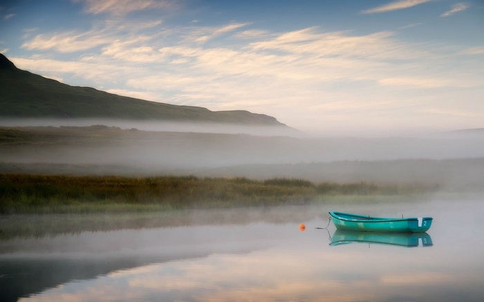 A teal rowboat floats on a misty lake