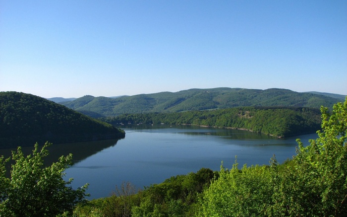 Lake surrounded by green hills under a clear blue sky