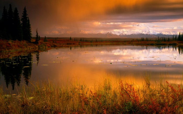 Lake reflecting snow-capped mountains at sunset