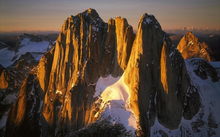 Golden hour illuminates jagged mountain peaks and snowy slopes