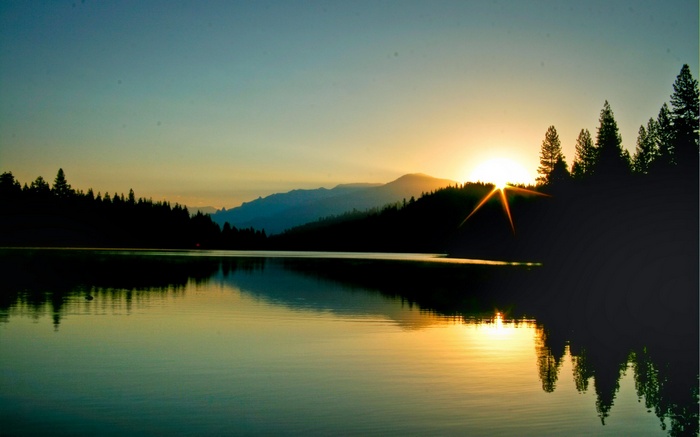 Sunset over a lake with silhouetted trees and mountains