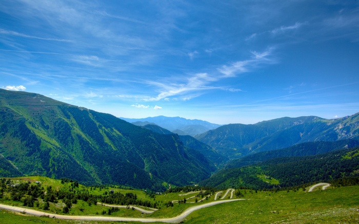 Winding mountain road through green valleys under a blue sky