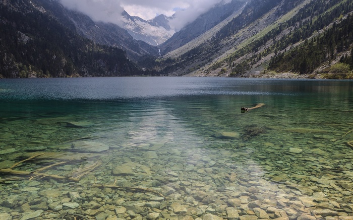 Clear mountain lake with rocky bottom and forested mountains