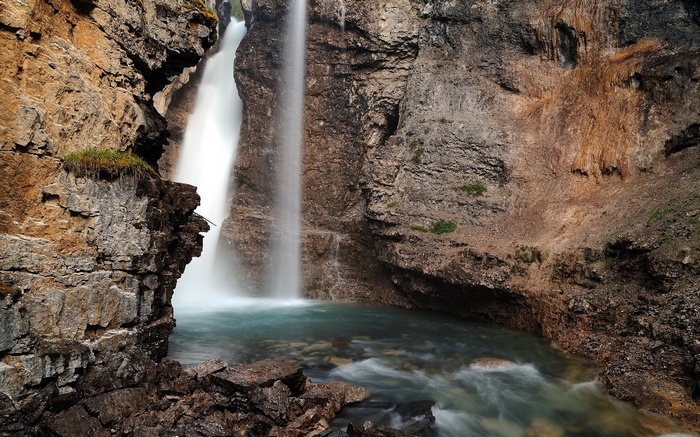 Waterfall cascading into a turquoise pool in a rocky canyon