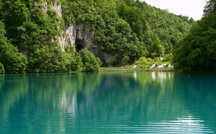 Turquoise lake with a cave and lush green forest