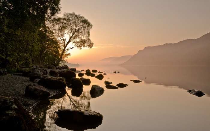 Sunrise over a misty lake with rocky shore and trees