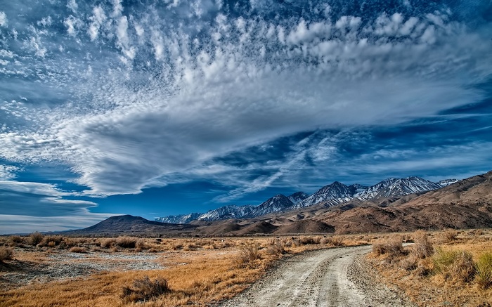 Dirt road leading to snow-capped mountains under dramatic clouds