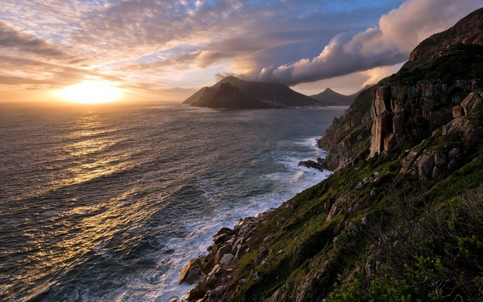 Sunset over a rocky coastline with mountains in the distance