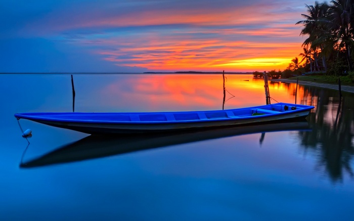 Blue boat on calm water at sunset with palm trees
