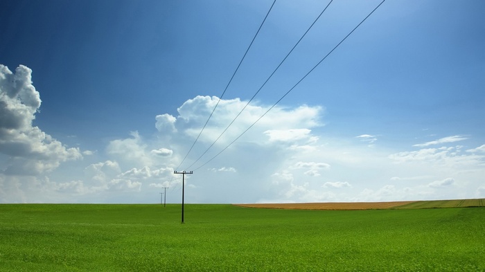 Power lines over a green field under a blue sky