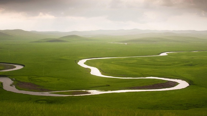 Winding river through green grasslands under cloudy sky
