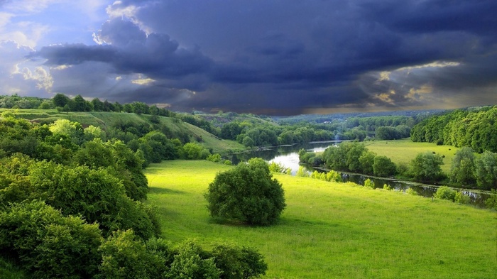 A river flows through a green valley under a stormy sky