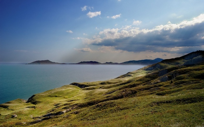 Rolling green hills meet the sea under a cloudy sky