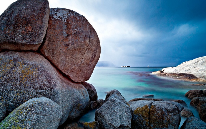 Large rocks on a beach with turquoise water and stormy sky