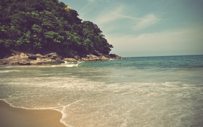Tropical beach with lush green hillside and ocean waves