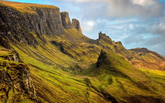 Rolling green hills and rocky cliffs under a cloudy sky