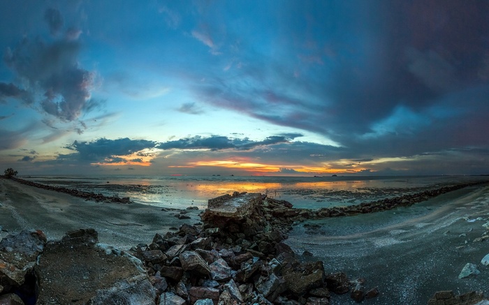 Panoramic sunset over a rocky beach with dramatic clouds