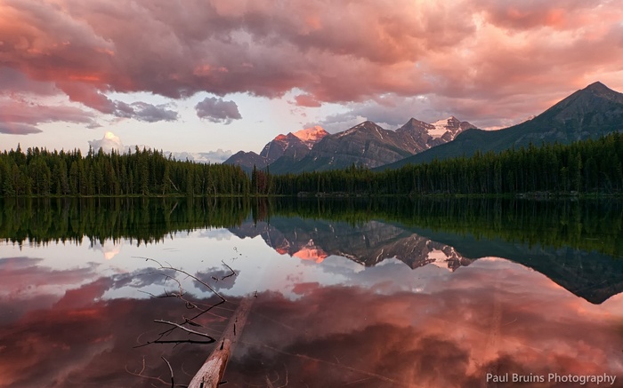 Sunset over mountains reflected in a lake with a fallen log