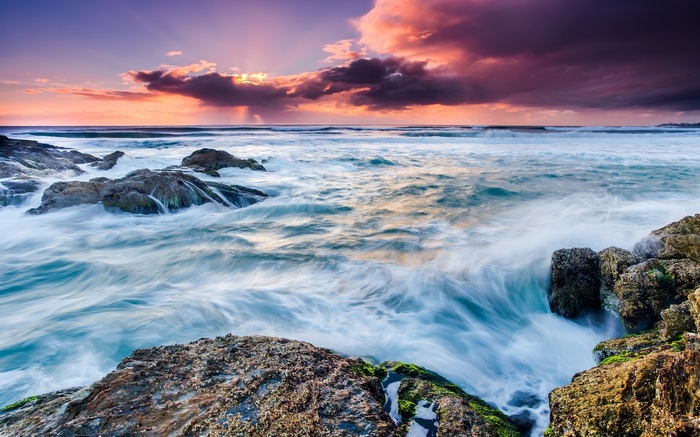 Ocean waves crashing on rocky shore at sunset