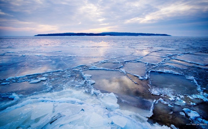 Cracked ice on a body of water with an island in the distance