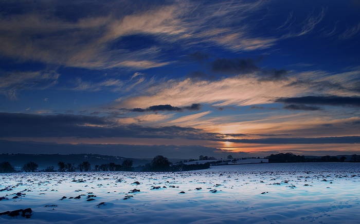 Snowy field at sunset with wispy clouds