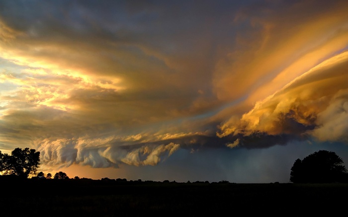 Dramatic storm clouds at sunset over a silhouetted landscape