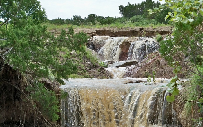 Muddy waterfall cascading over rocks with trees