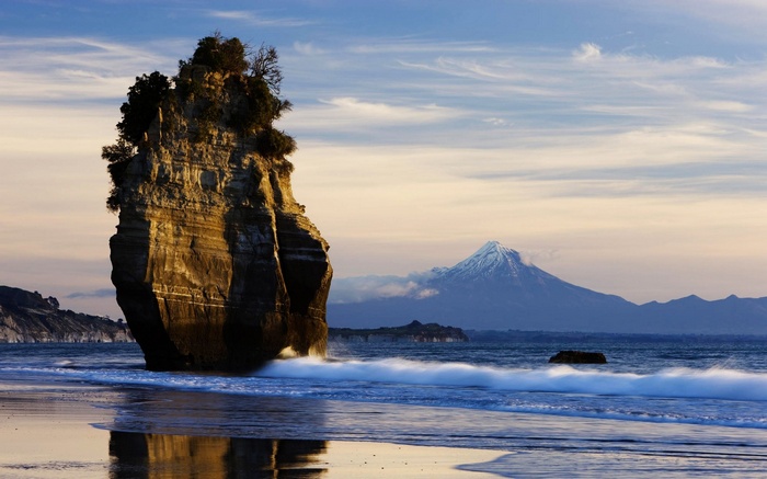 Rock formation on a beach with a snow-capped mountain in the background