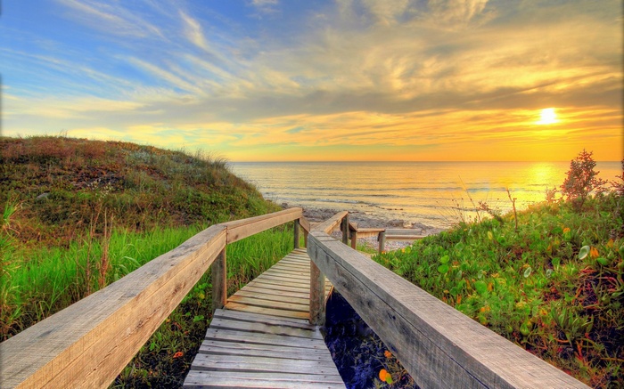 Wooden boardwalk leading to the ocean at sunset
