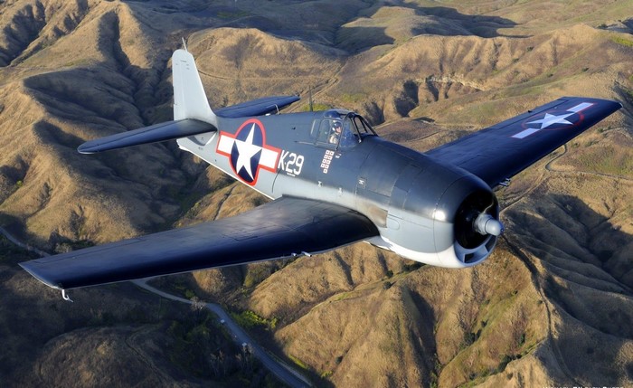 Grumman F6F Hellcat fighter plane flying over hills