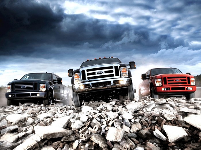 Three Ford trucks driving over rubble