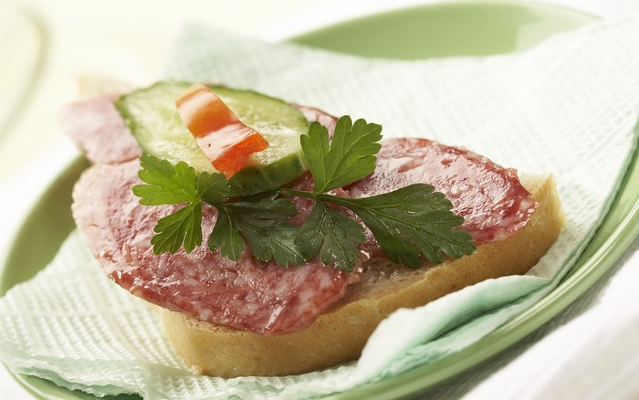 Sandwich with salami, cucumber, and parsley on a plate