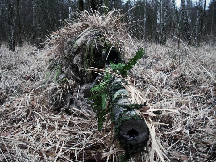 Soldier in ghillie suit with sniper rifle in forest