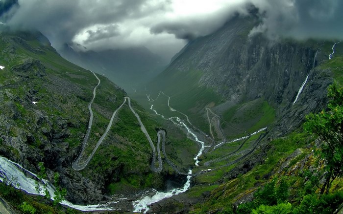 Winding mountain road with waterfalls and clouds