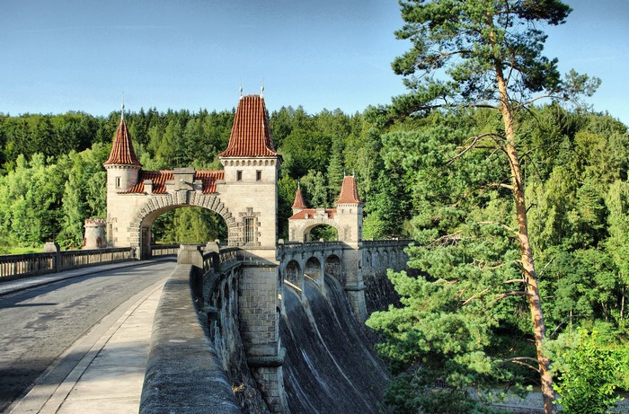 Stone dam with castle-like towers and a forest background