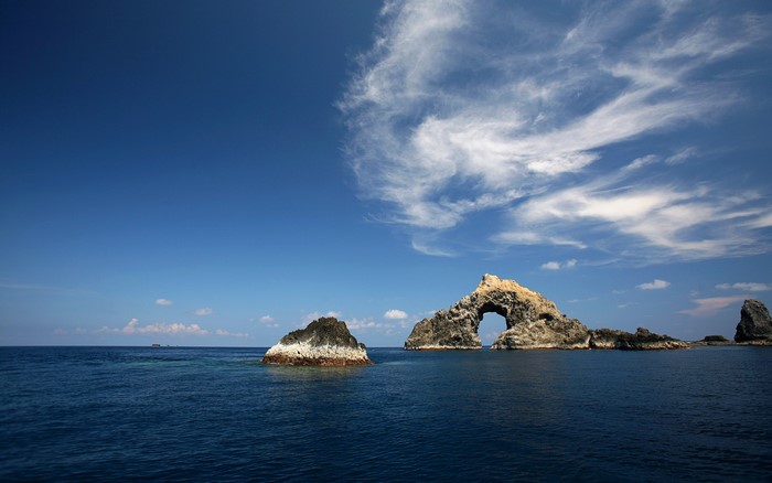 Arch rock formation in the open sea under a blue sky