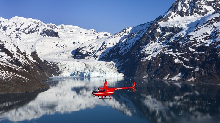 Red helicopter flying over a glacier and mountains