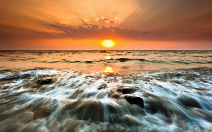 Sunset over the ocean with waves crashing on rocks