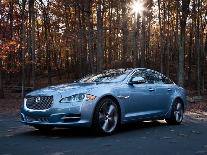 Blue Jaguar XJ driving on a road in autumn forest