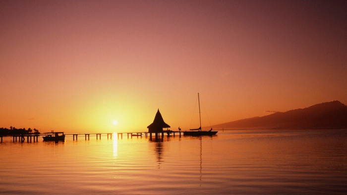 Sunset over the ocean with a pier and sailboat