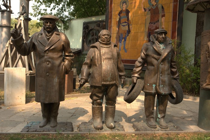 Three bronze sculptures of men in coats