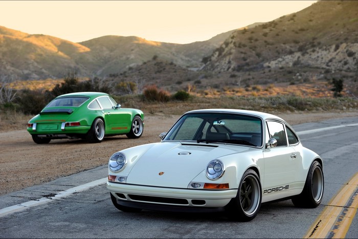 Two Porsche 911s on a road with mountains
