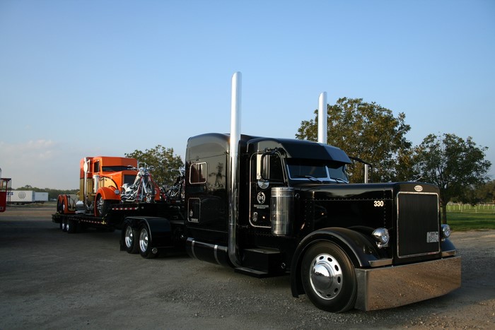 Black Peterbilt 330 truck hauling an orange truck and motorcycles