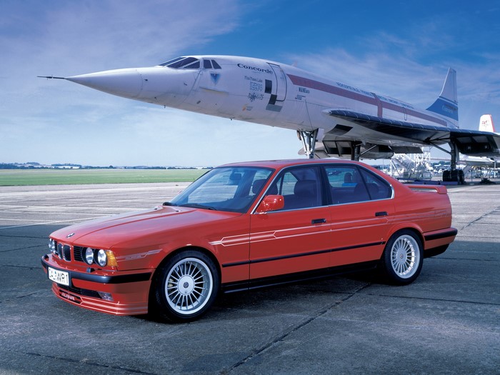 Red BMW car parked in front of Concorde airplane