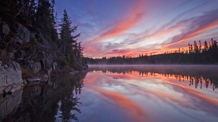 Sunrise over a misty lake with rocky shore