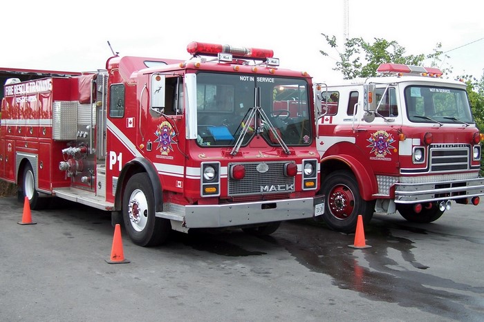 Two red fire trucks, one Mack and one International, parked outside.